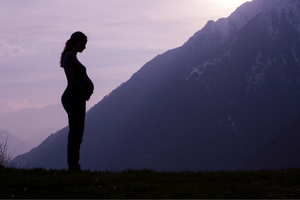 Silhouette of pregnant woman standing before a mountain